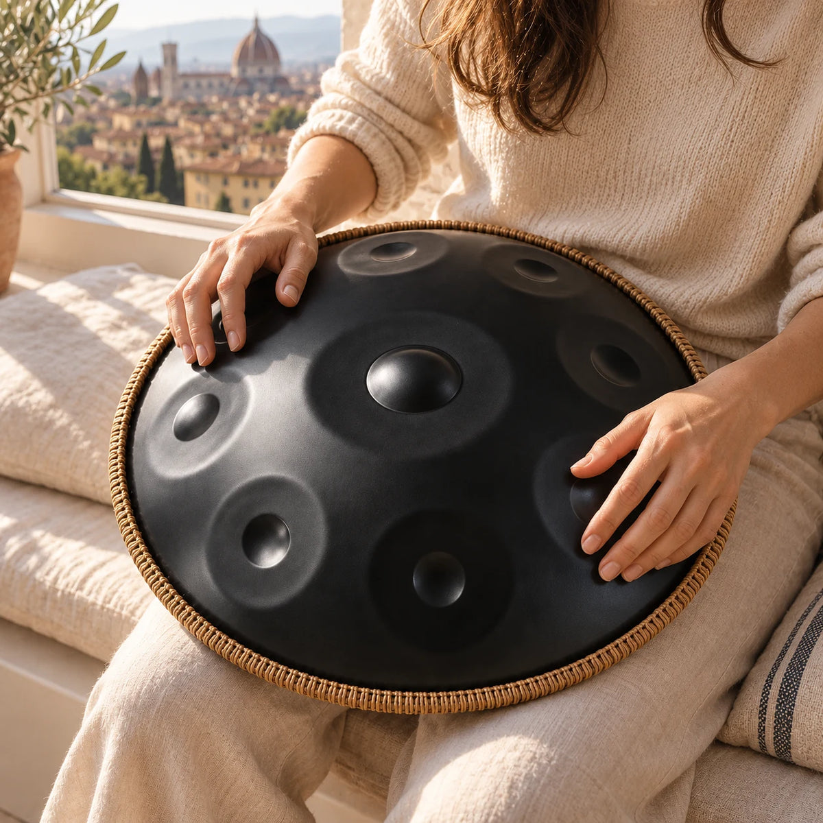 Handpan Risuono Ombra nero opaco con bordo intrecciato mentre lo si suona vicino a una finestra su Firenze