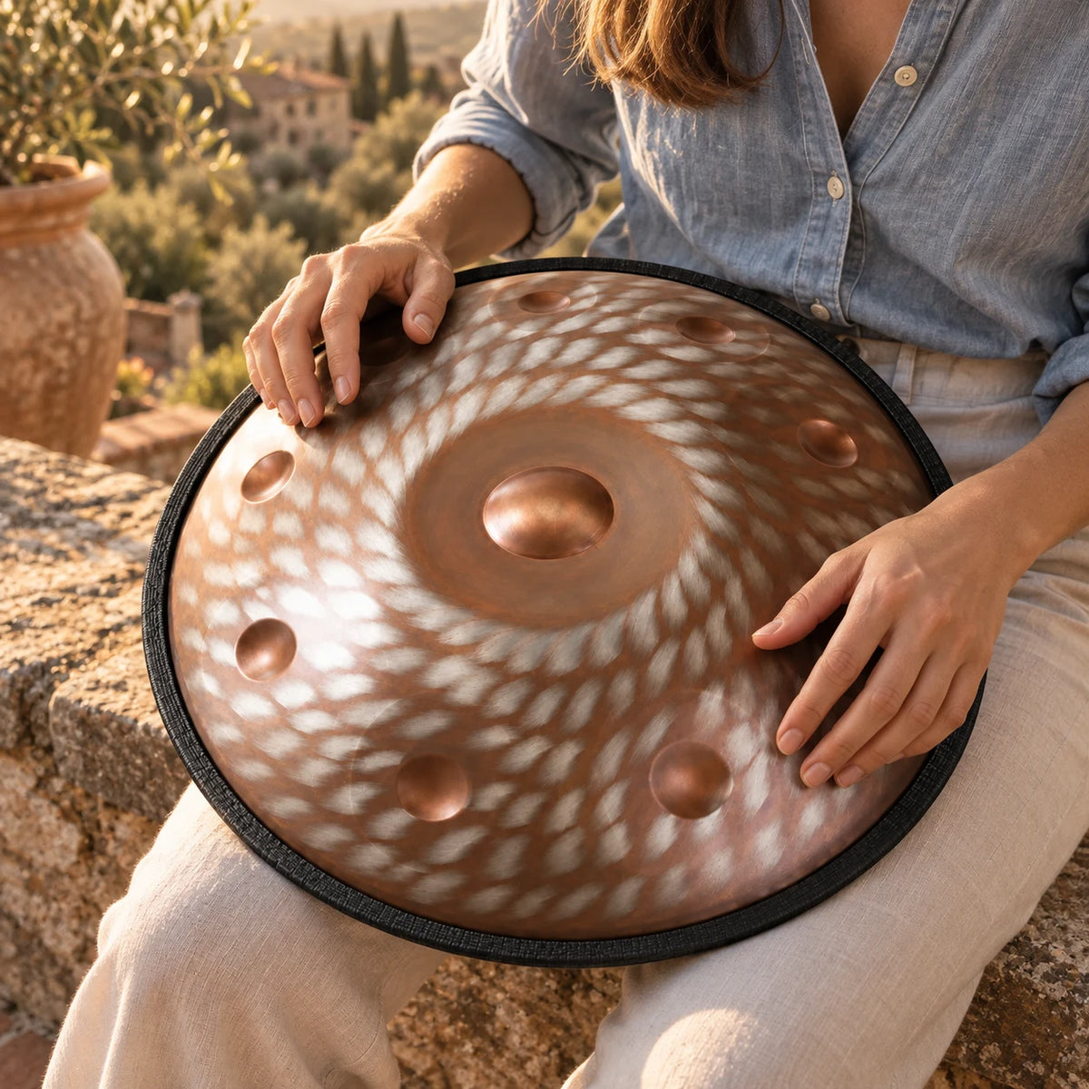 Handpan Risuono Brace ramato con motivo a spirale mentre lo si suona su una terrazza toscana